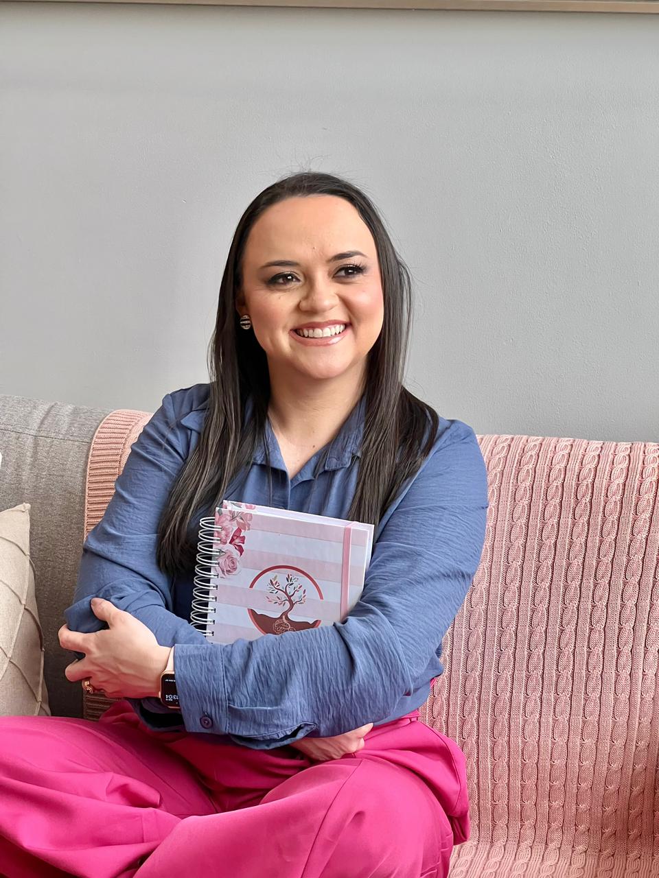 Daniela Pereira sentada em um sofá segurando o caderno da marca